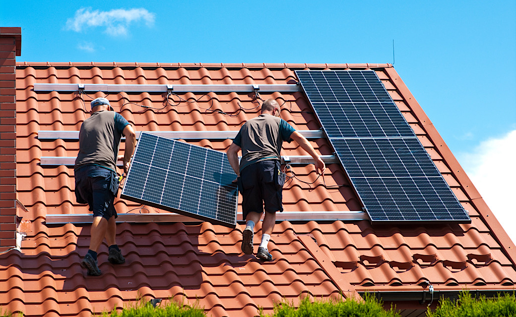 Two men installing new solar panels on the roof of a private house.