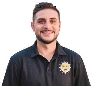 A smiling man with short dark hair and a neatly trimmed beard, wearing a black polo shirt with a Sunlight Electrical logo. The background is transparent, focusing on his upper body.