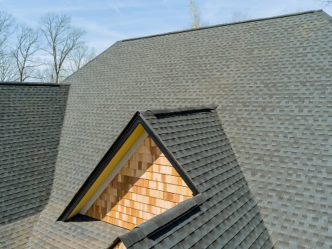 Close-up view of a residential roof with a dormer featuring cedar shingle siding and dark roof shingles.