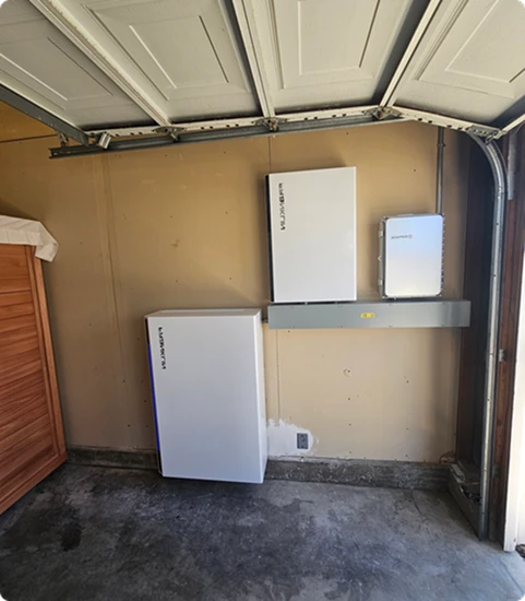 Home battery storage system with wall-mounted inverters and energy management equipment in a residential garage.